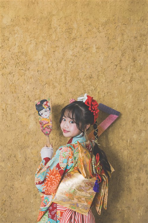 きいろ背景で羽子板を持つ七五三写真