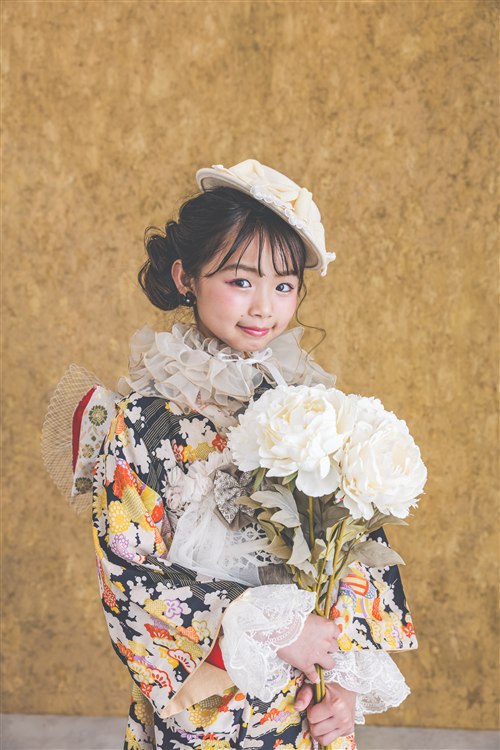 きいろ背景で花を持つ七五三写真